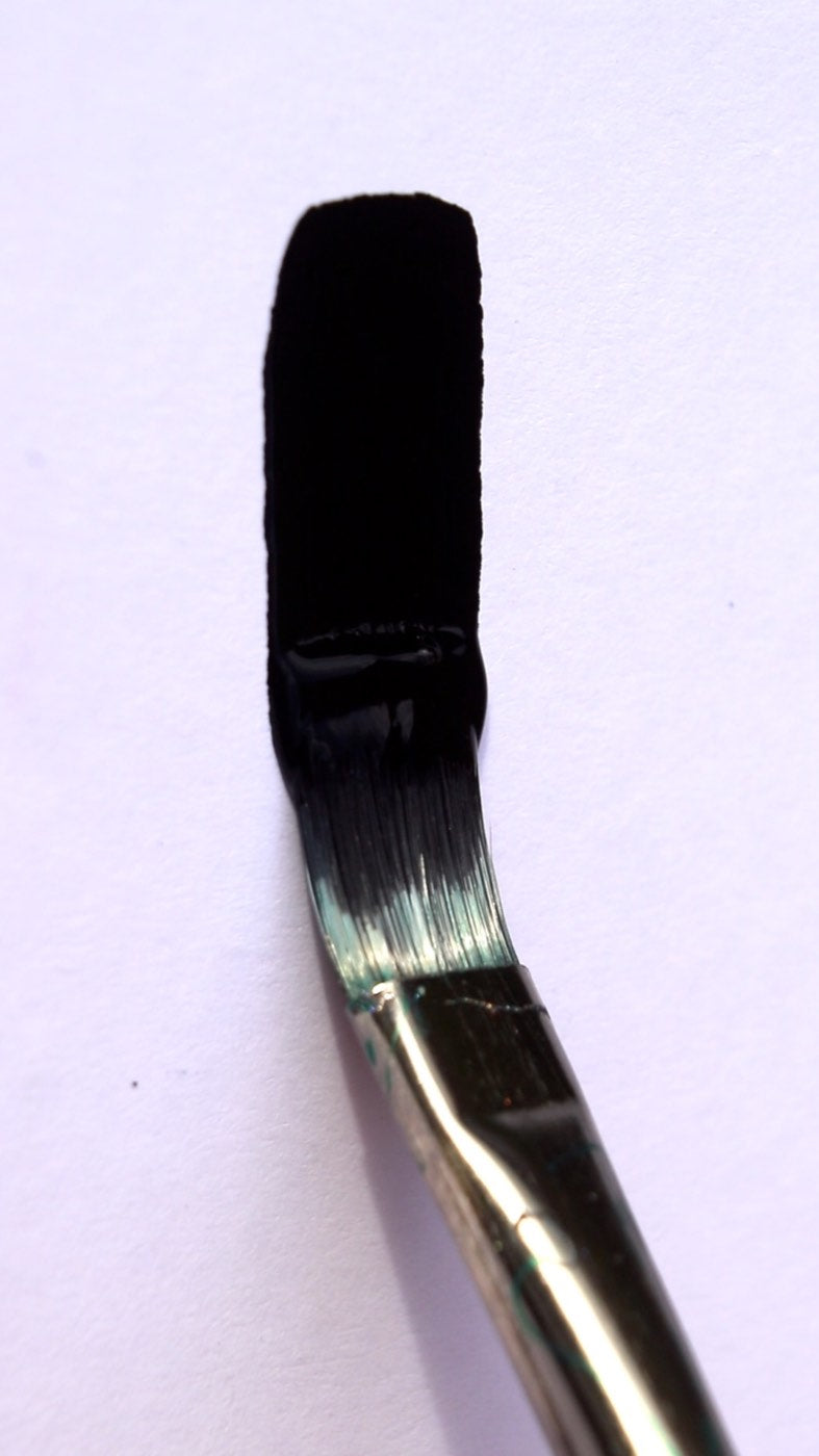 A flat brush loaded with black paint above a painted black square