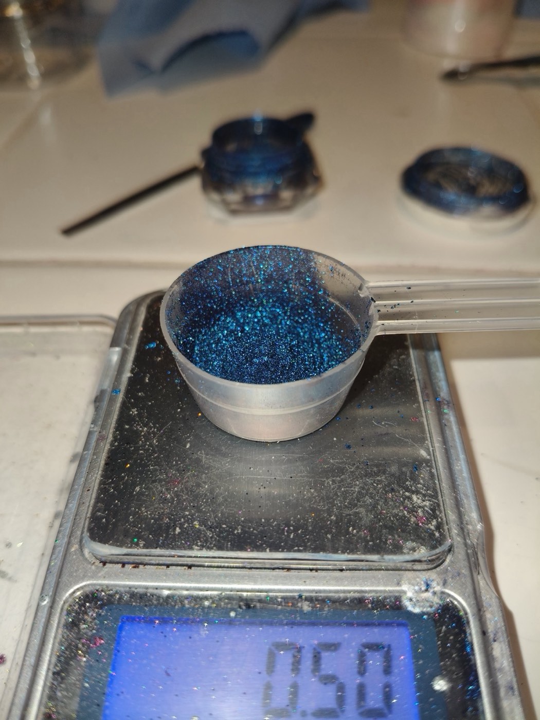 Blue glitter pigment in a measuring cup on a digital scale