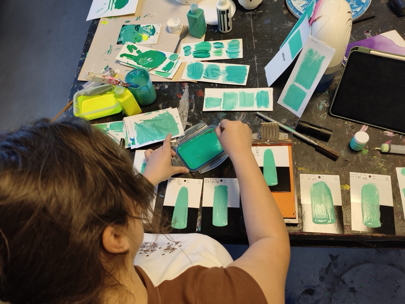 A person at a studio table painting green test swatches onto cards