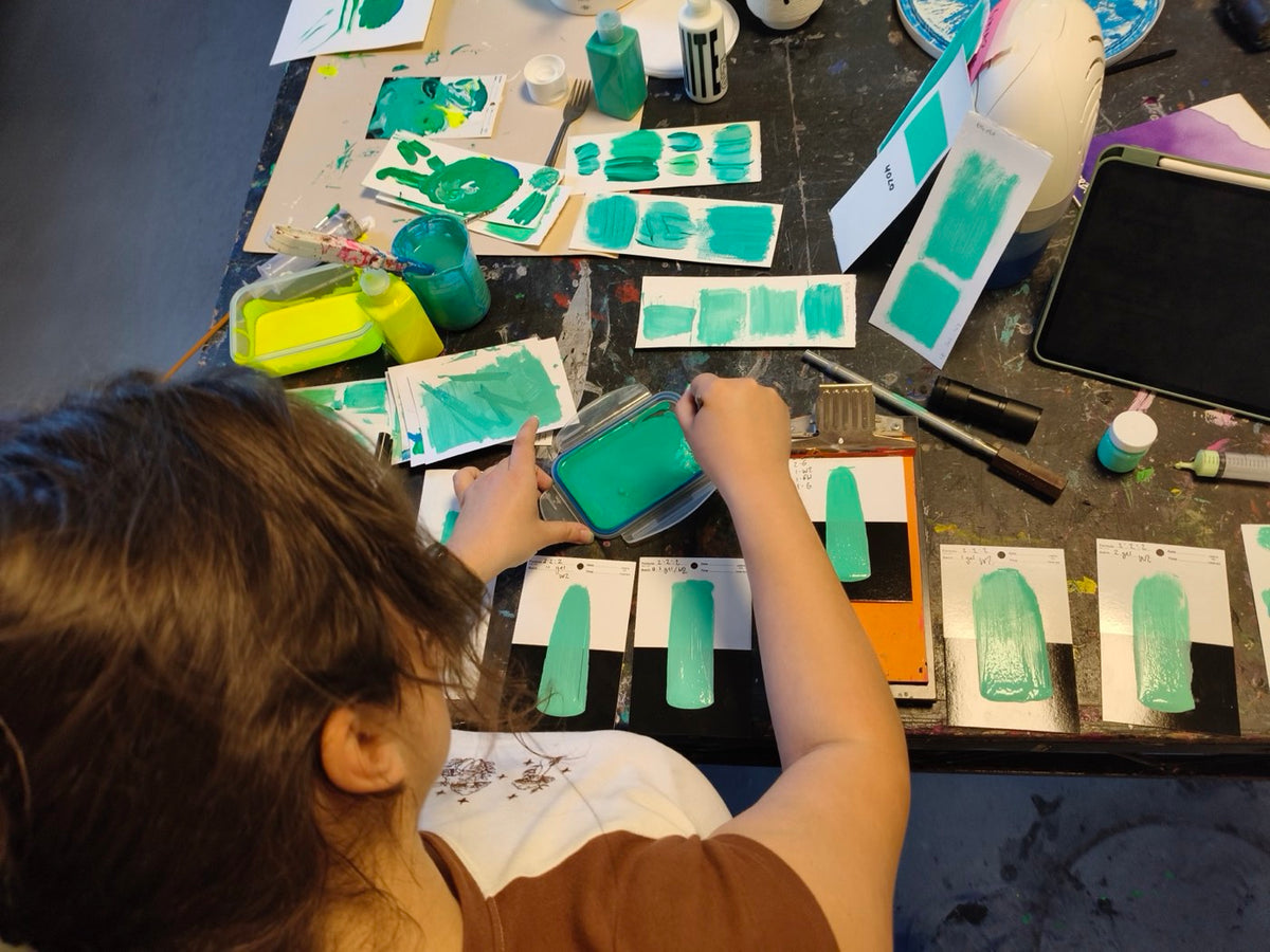 A person at a studio table painting green test swatches onto cards