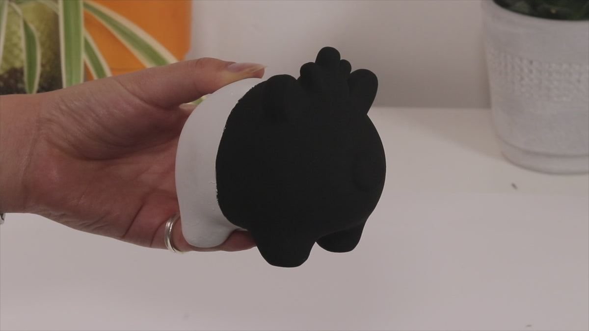 A hand turning a small pig sculpture half painted in Black 4.0, the black side losing all its shape